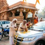 Devotees performing vehicle pooja with cars and bikes outside a temple.