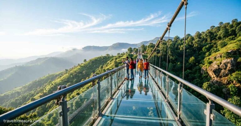 Glass walkway of Rajgir Glass Bridge over green hills with visitors walking across.